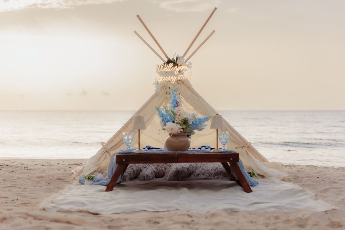 Boho tepee with an illuminated sign at sunset on the beach