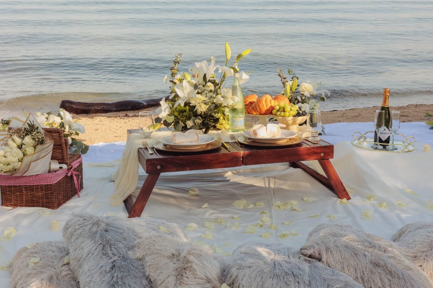 Table set with gold glassware, croissants and white florals on the beach