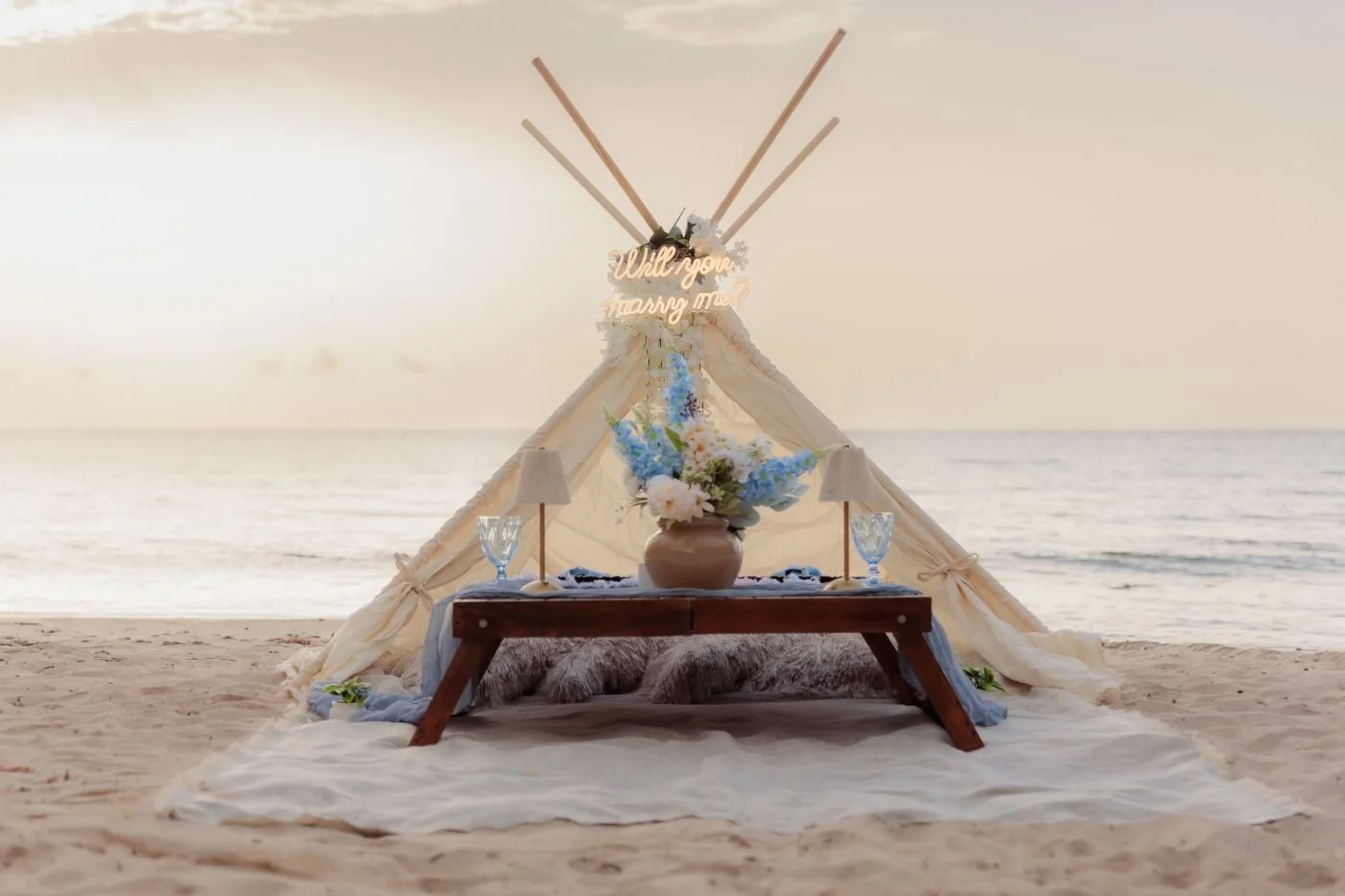 Boho tepee with an illuminated sign at sunset on the beach