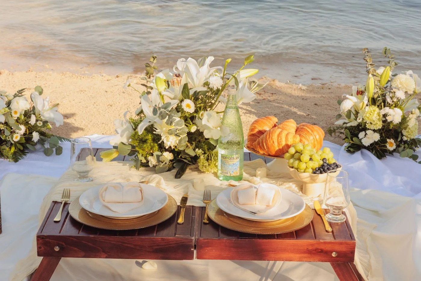 White and gold setup facing the sea in Cozumel, with a low table, cushions and florals